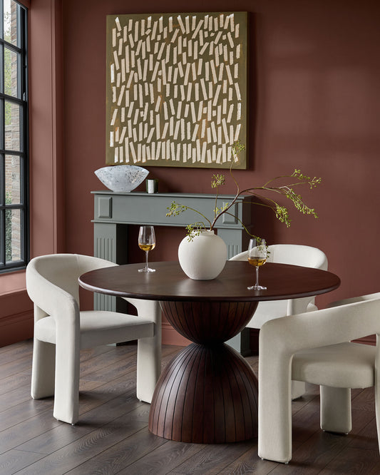 Cream fabric dining chair with curved, sculptural armrests and legs, shown in dining room setting.