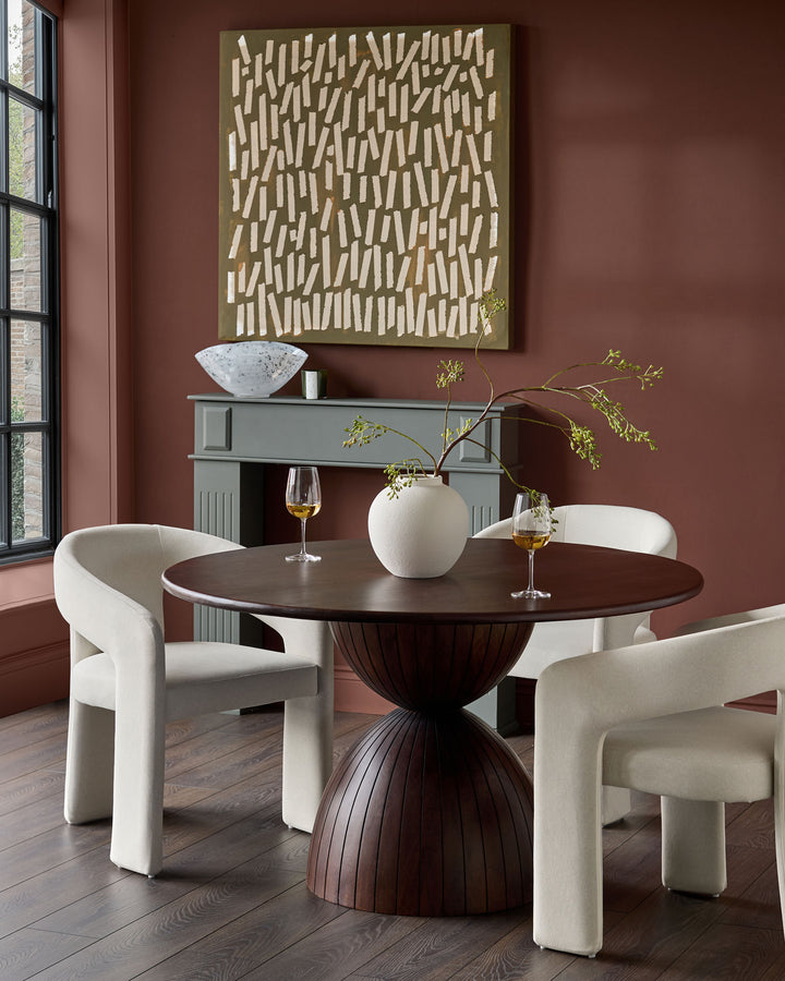 Cream fabric dining chair with curved, sculptural armrests and legs, shown in dining room setting.