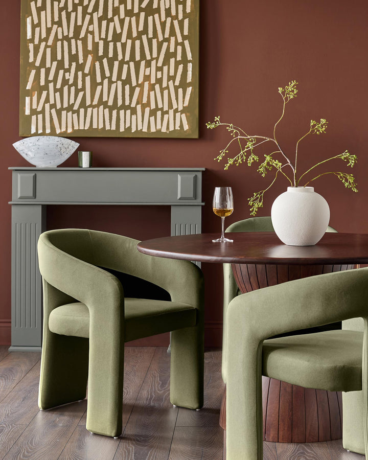 Olive green Asher dining chair with curved, sculptural arms and upholstered seat, shown in a styled room setting.