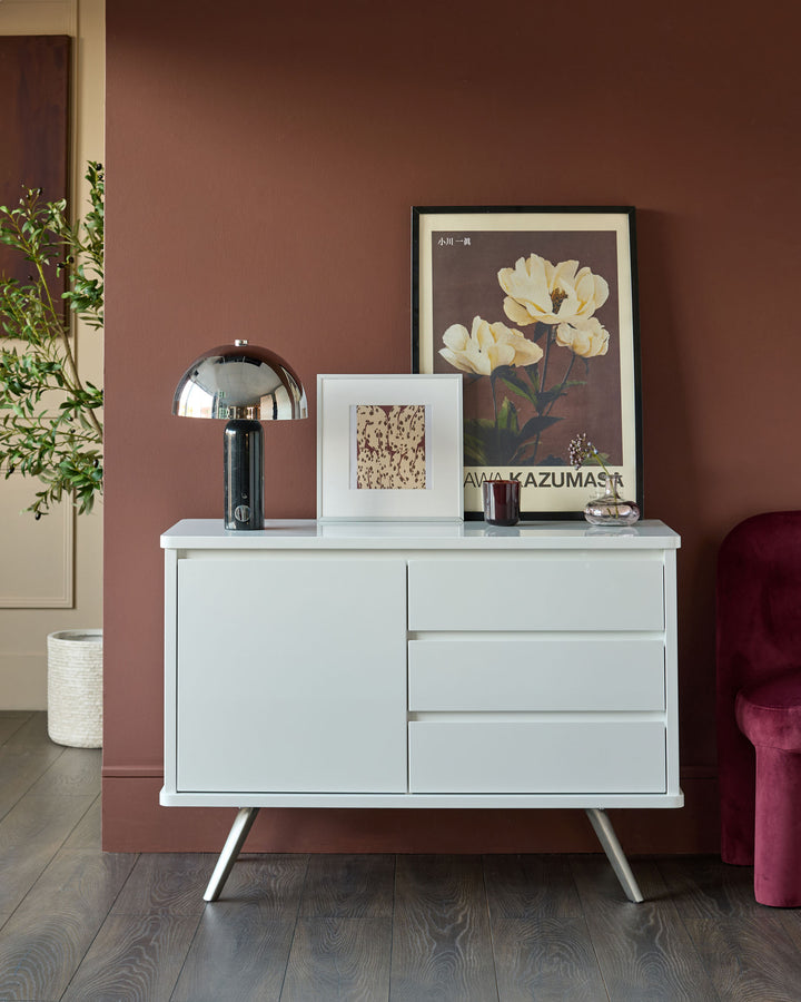 White gloss compact sideboard with angled metal legs, featuring one door and three drawers in a modern mid-century style.