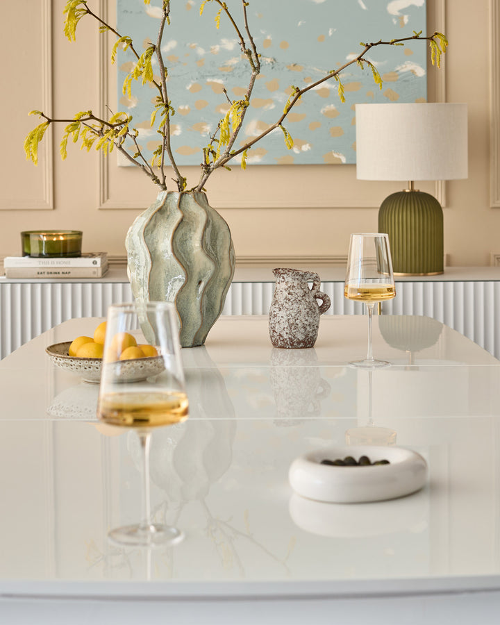 White extending dining table styled with decorative vase, lamp, and tableware in a modern interior setting.