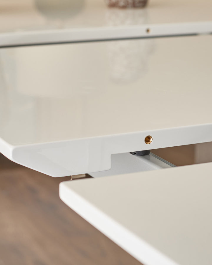 Close-up of white extending dining table showing copper handle detail and extension mechanism.