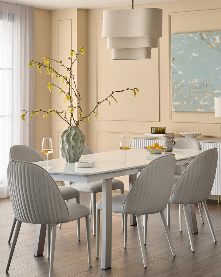 White extending dining table with metal legs, seated with four gray upholstered chairs in a modern dining room setting.