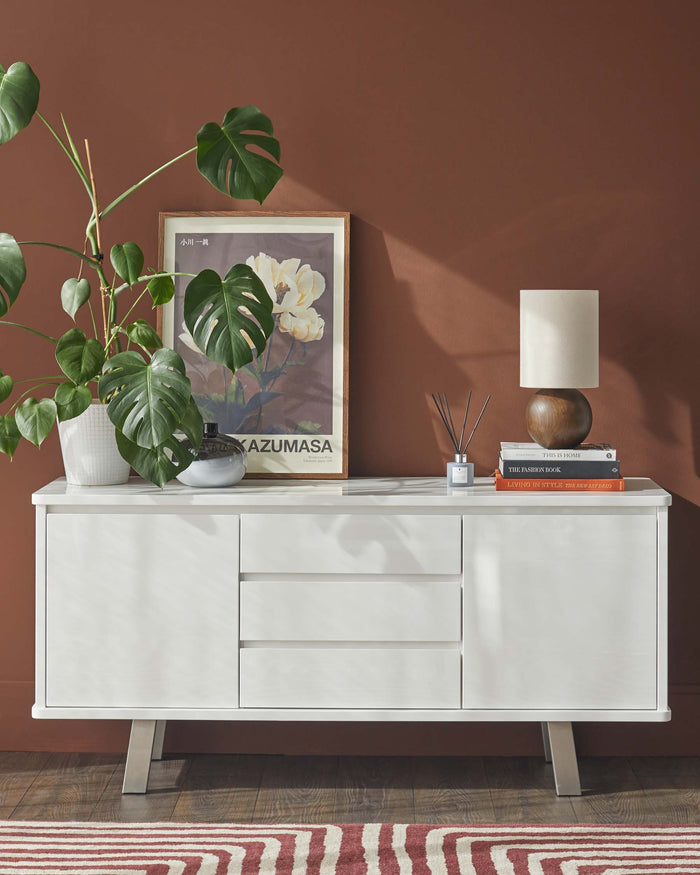 A modern white sideboard with storage drawers and a cabinet, accessorised with decorative items.