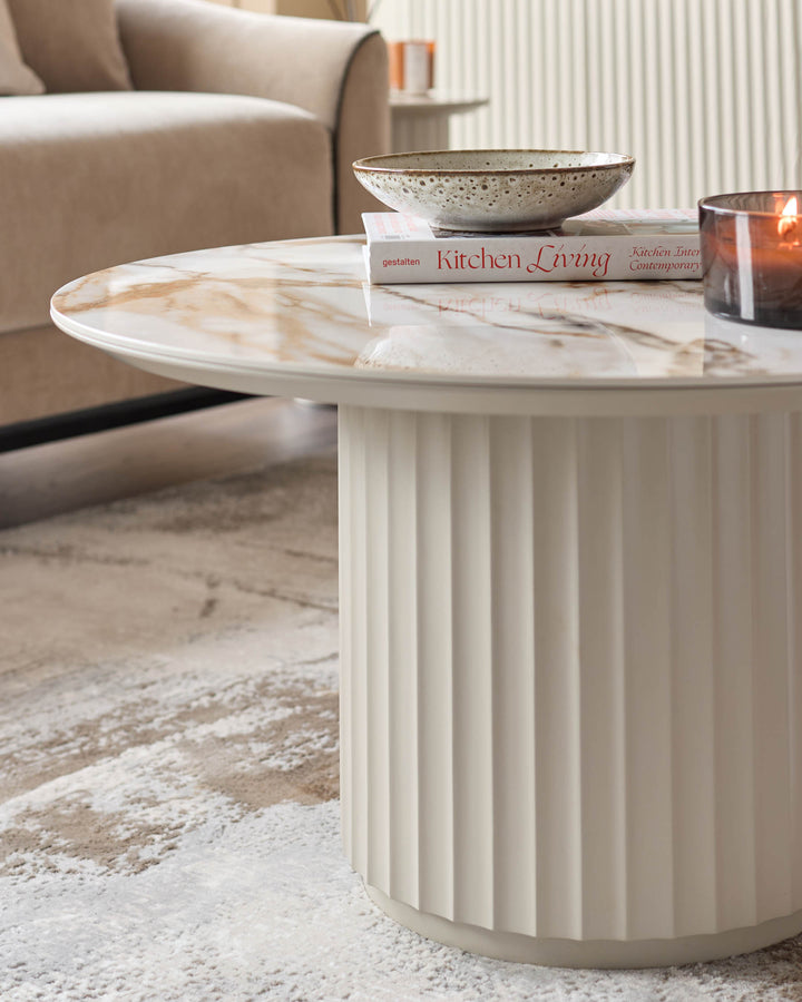 A stylish marble-topped coffee table with a reeded base, displaying books, a bowl and candle, adds a touch of elegance to any living space.