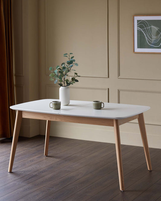 A stylish dining table with a white top and light wood legs, complemented by minimalist decor and warm, neutral tones.