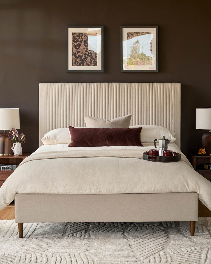 Cream fabric king-size bed with vertical ribbed headboard and wooden legs, displayed in a styled bedroom setting.