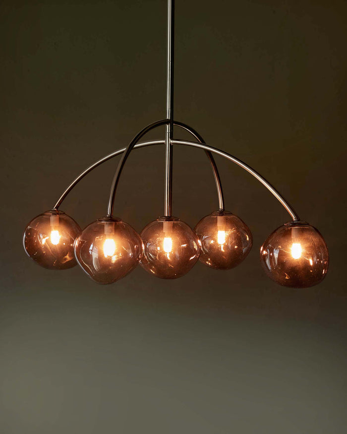 A statement chandelier featuring five warm-toned, illuminated glass globes suspended from a sleek, curved metal frame.