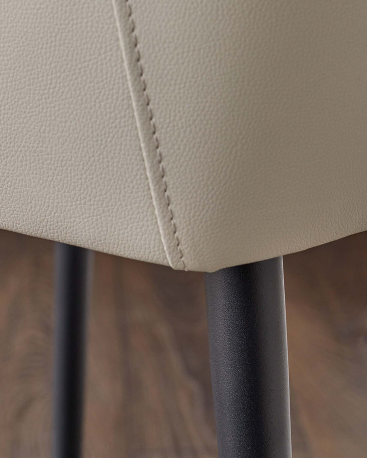 Close-up of a chair with light grey leather upholstery and black metal legs, showcasing texture and design details.