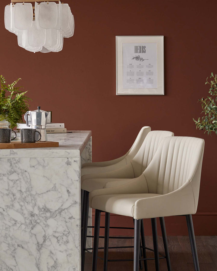 Elegant kitchen with marble island, cream bar stools with black legs, and stylish chandelier.