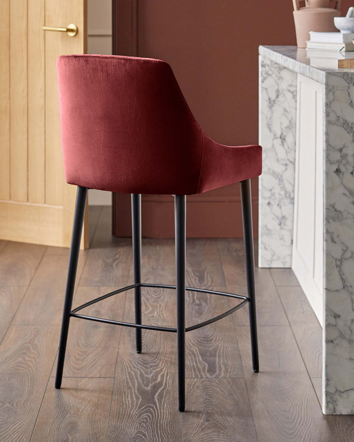 A velvet bar stool in a muted, deep red with sleek, black metal legs sits on a wooden floor by a marble-topped counter.