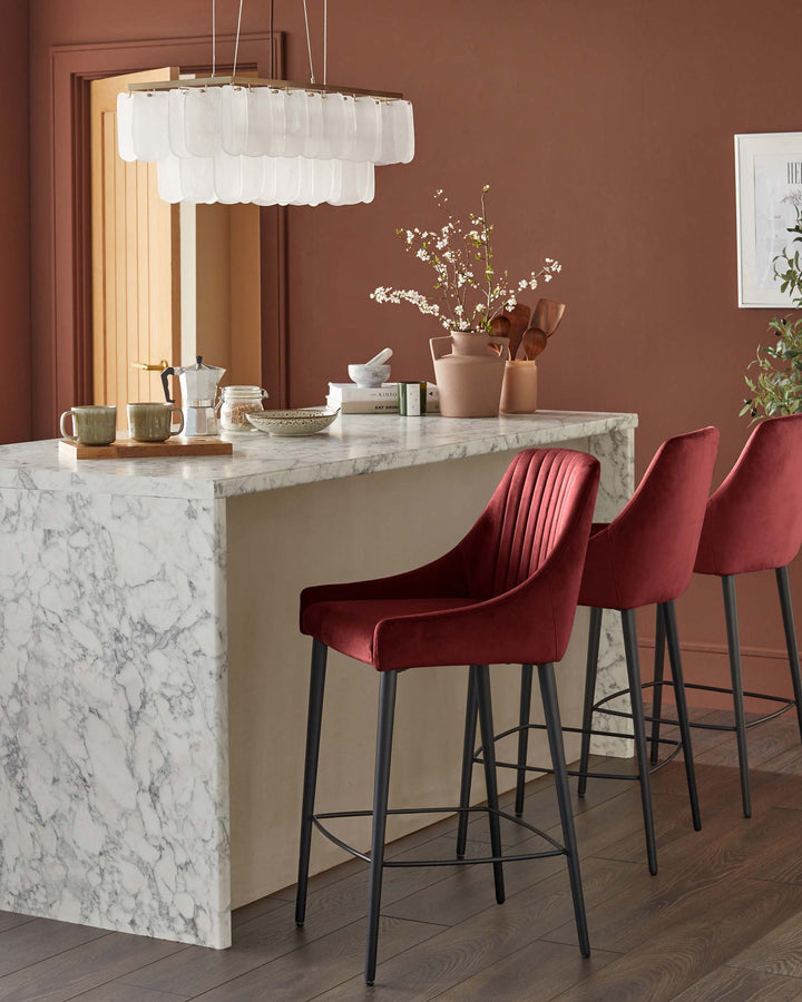 A kitchen island with marble worktop and three red velvet bar stools with black legs in a modern, stylish kitchen.