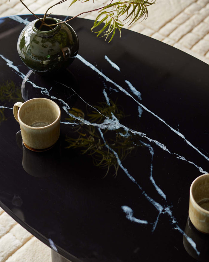 A sleek black marble table displays a vase and two mugs, reflecting light and texture in a contemporary setting.