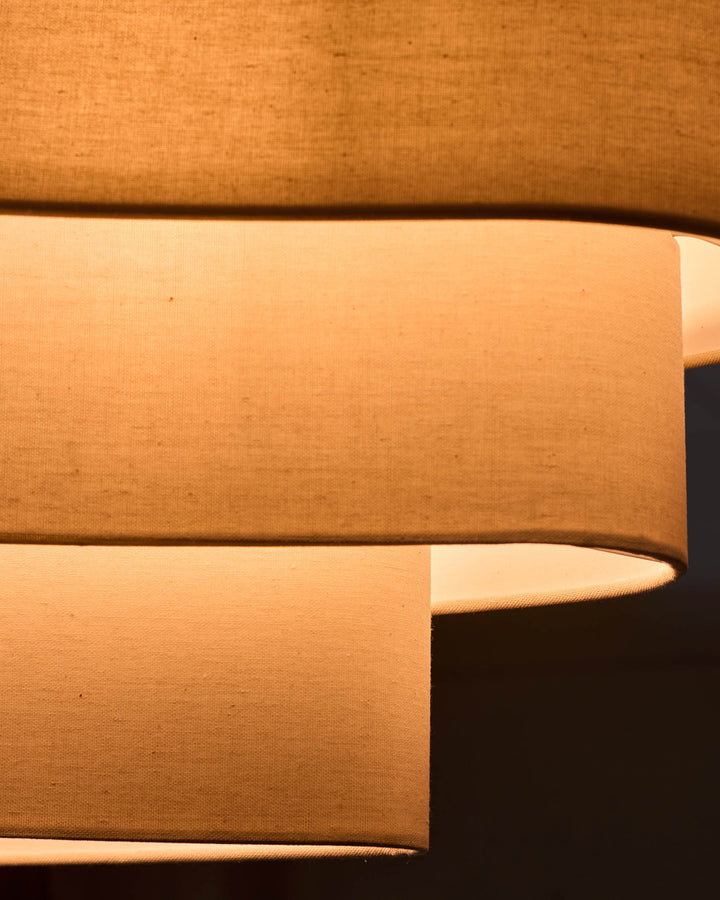 Natural linen pendant light with two cylindrical shades in warm beige, shown at an angle highlighting the fabric texture and form.