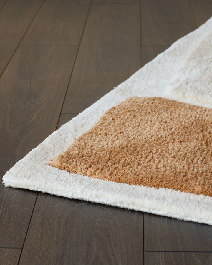 Close-up of a patterned shag rug in cream and brown on a dark wooden floor. Ideal for adding texture and warmth to any room.