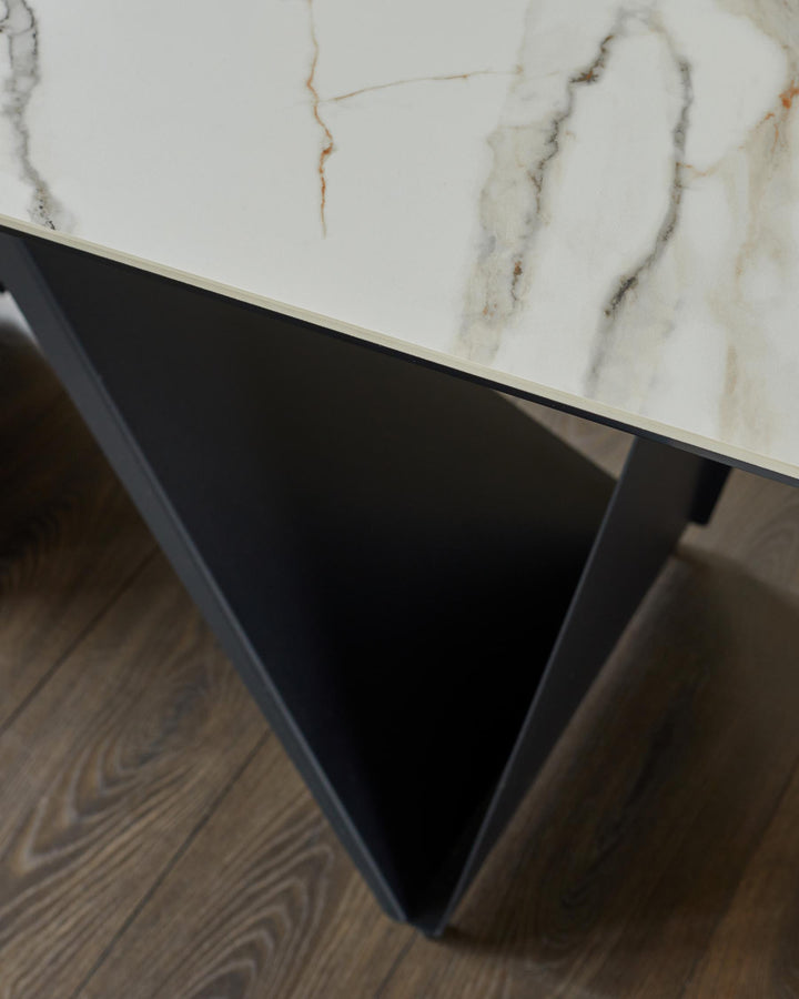 A modern coffee table with a white marble effect top and black angular legs, sat on a brown wooden floor.