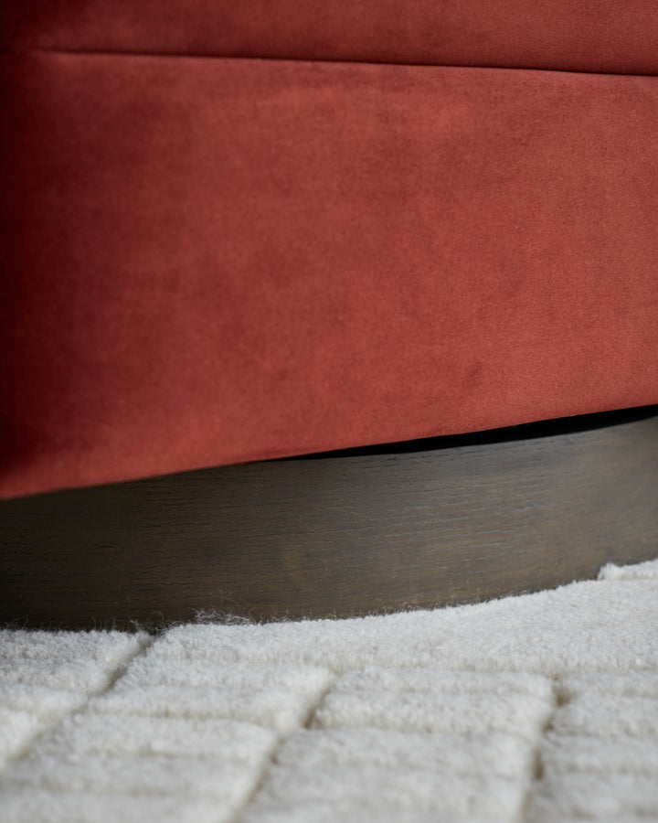 Close-up of a stylish, contemporary red sofa with a dark wood base, sitting on a textured, light-coloured rug.