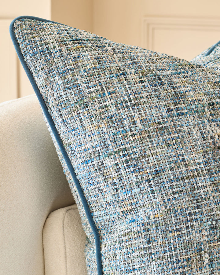 Large blue textured cushion with woven fabric detail, displayed on a cream upholstered chair arm.