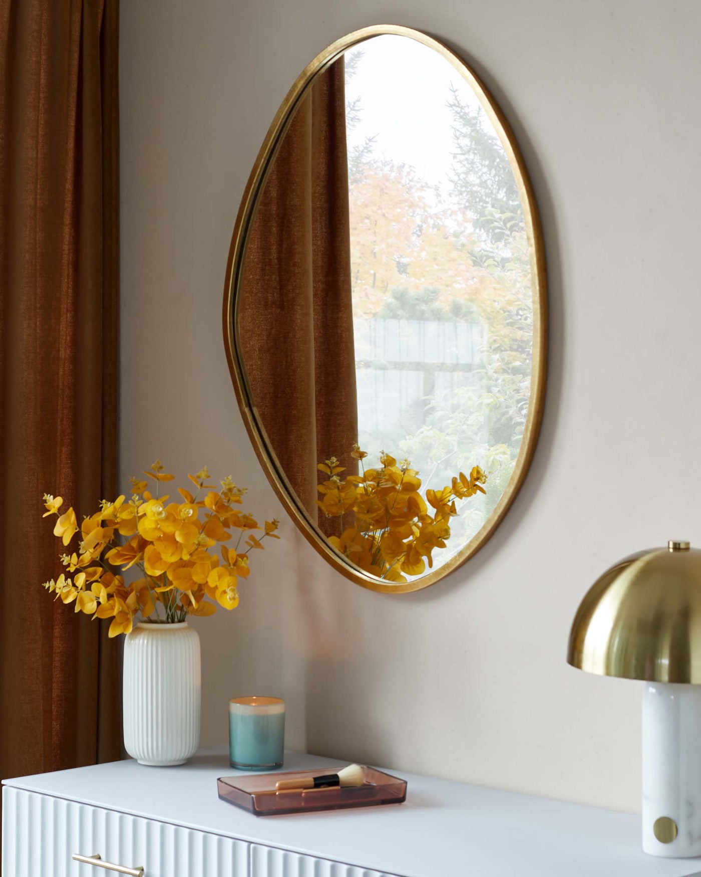A sleek, modern white console table with textured front panels, featuring minimalist golden handles and a smooth, flat top surface. A round mirror with a thin, golden frame hangs above it.