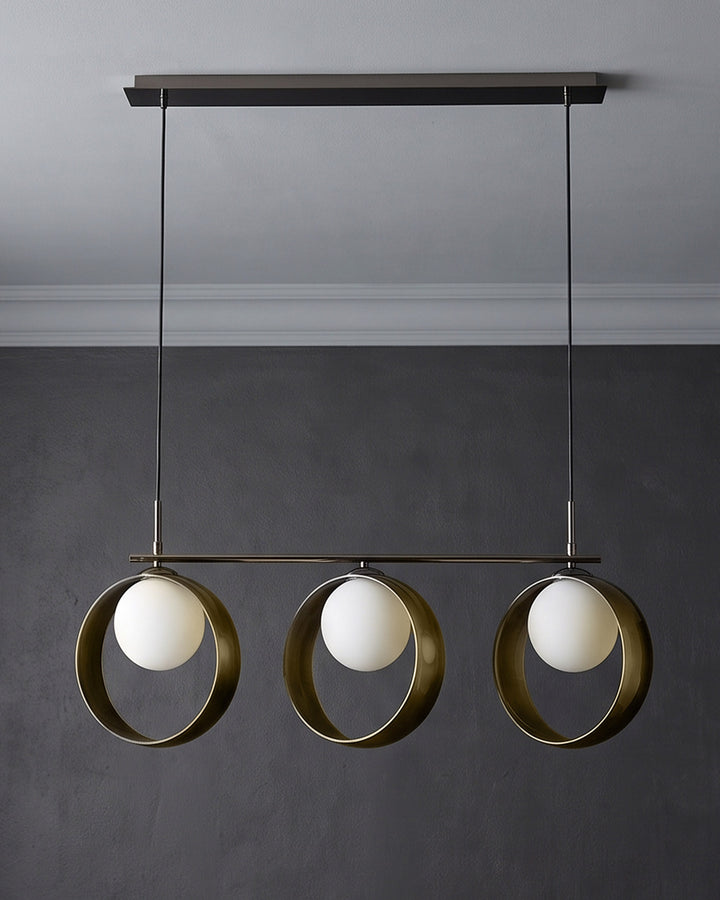 Chloe 3-pendant light with green metal rings and white spherical glass shades, suspended from dark ceiling fixture.