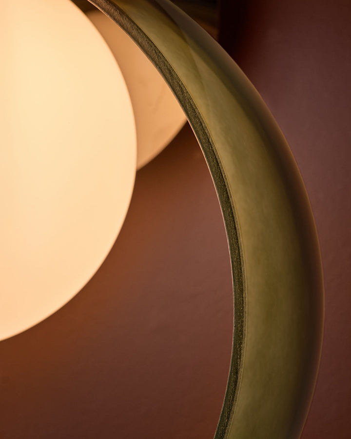 Green glass wall light with curved organic shape, close-up detail showing textured edge and warm ambient glow.