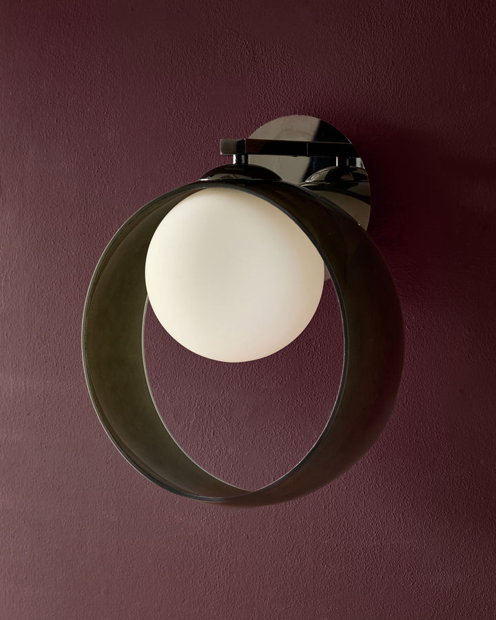 Modern wall sconce with circular opal glass diffuser and black metal frame mounted on burgundy wall.