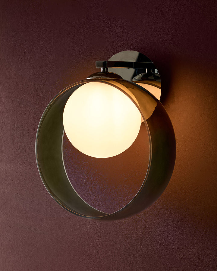 Chloe wall light with circular green glass shade and chrome fixture, illuminated against burgundy wall.