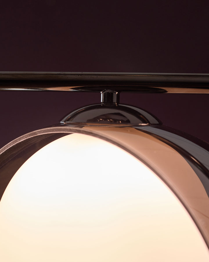 Chrome pendant light with frosted glass globe shade, viewed from below against dark background, showing metallic fixture and warm glow.