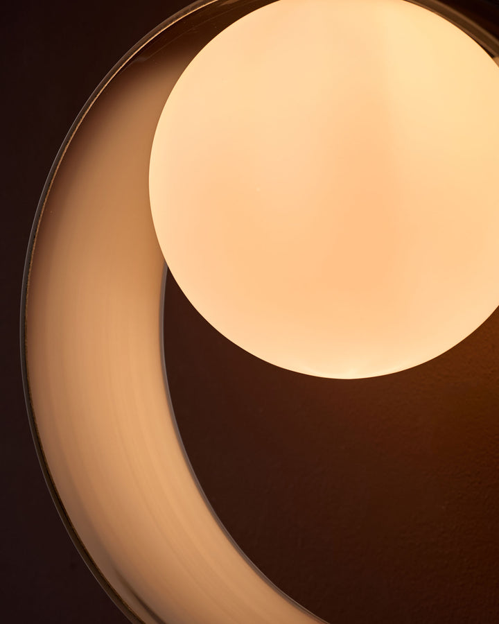 Chloe wall light with curved chrome handle and illuminated cream glass globe against dark background.
