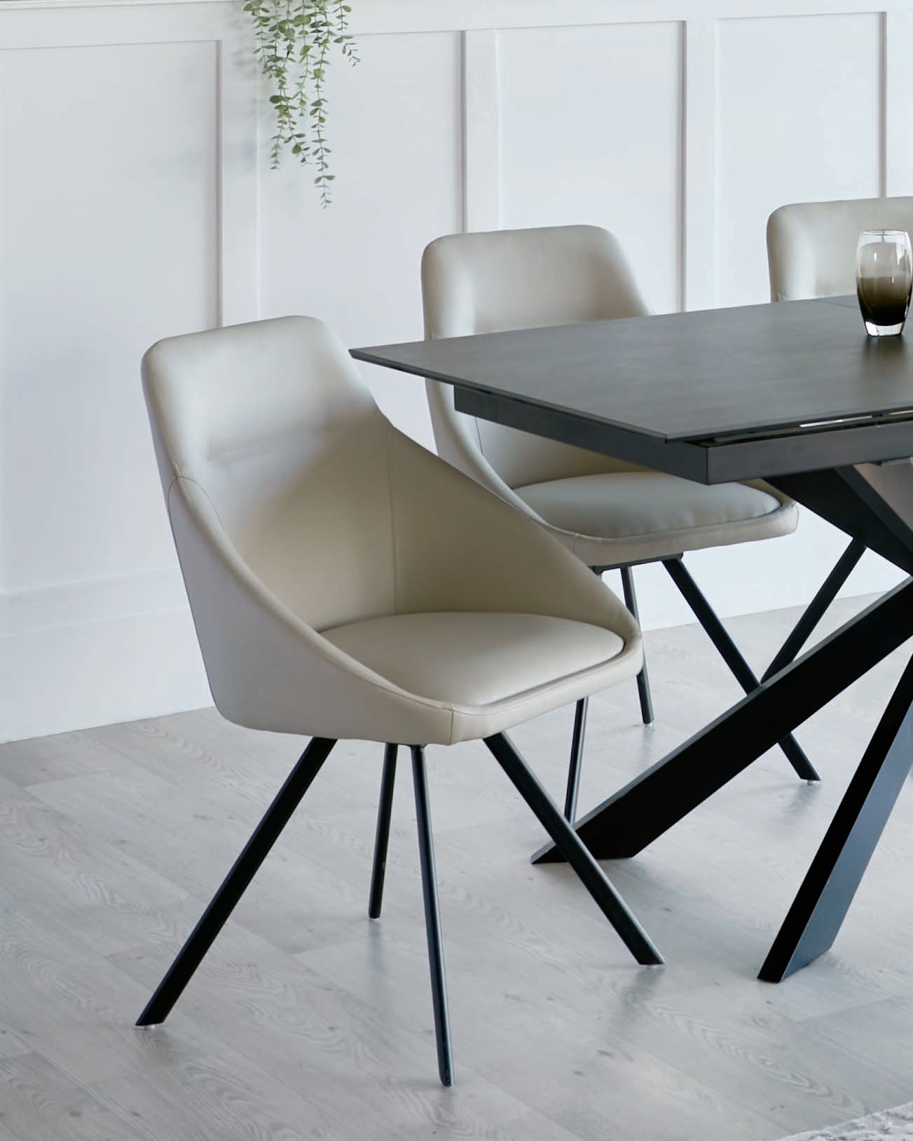 Modern minimalist dining room furniture featuring a dark wood table with a sleek, black frame and angular legs, accompanied by light grey upholstered chairs with comfortable curved backs and slender, tapered black metal legs.
