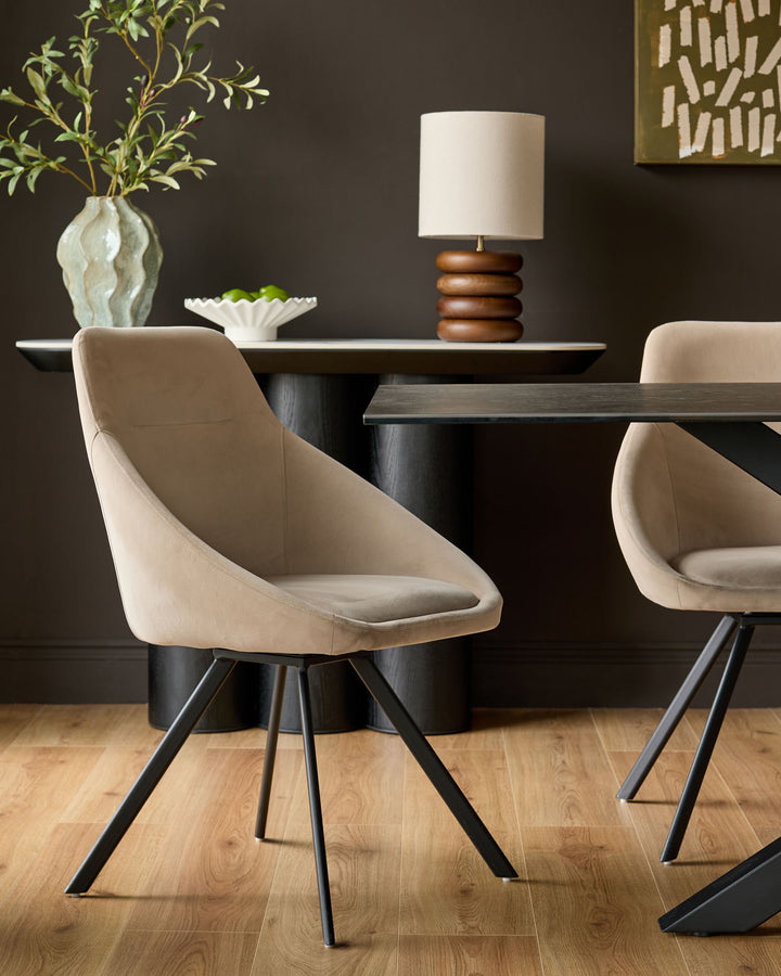 Champagne velvet swivel chair with curved bucket seat and black metal legs, shown in dining room setting.