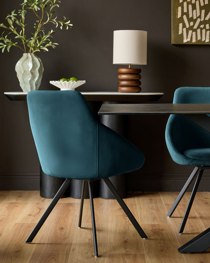 Cleo velvet swivel chair in dark teal with black metal legs, shown in dining room setting at table.