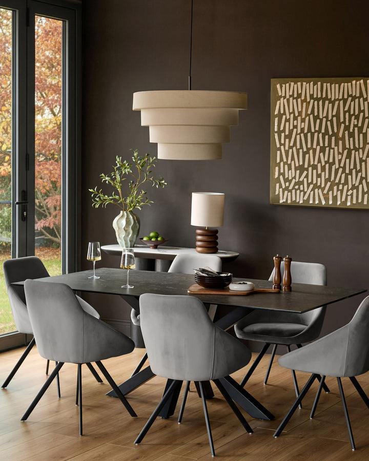 Cleo velvet swivel chair in dark grey, shown in modern dining room setting with table and pendant lighting.