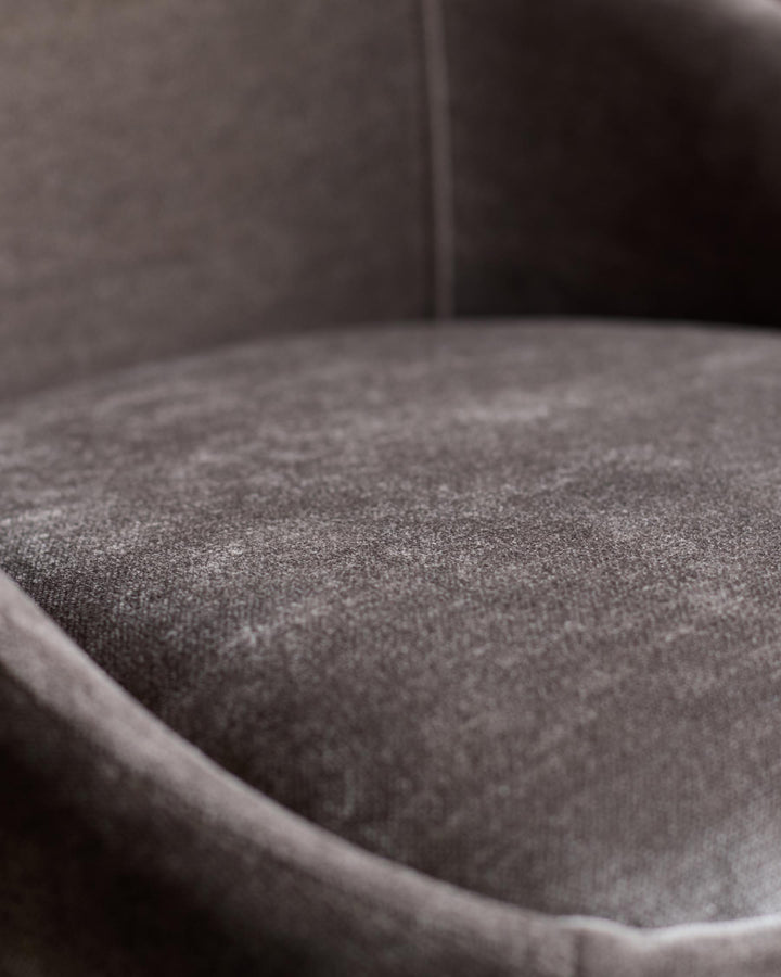 Close-up of a plush, curved chair in a warm, muted tone. The textured fabric seat invites relaxation.
