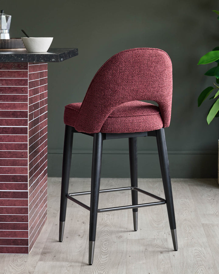 A stylish counter stool with a burgundy fabric seat and back, and dark wooden legs with a metal footrest.