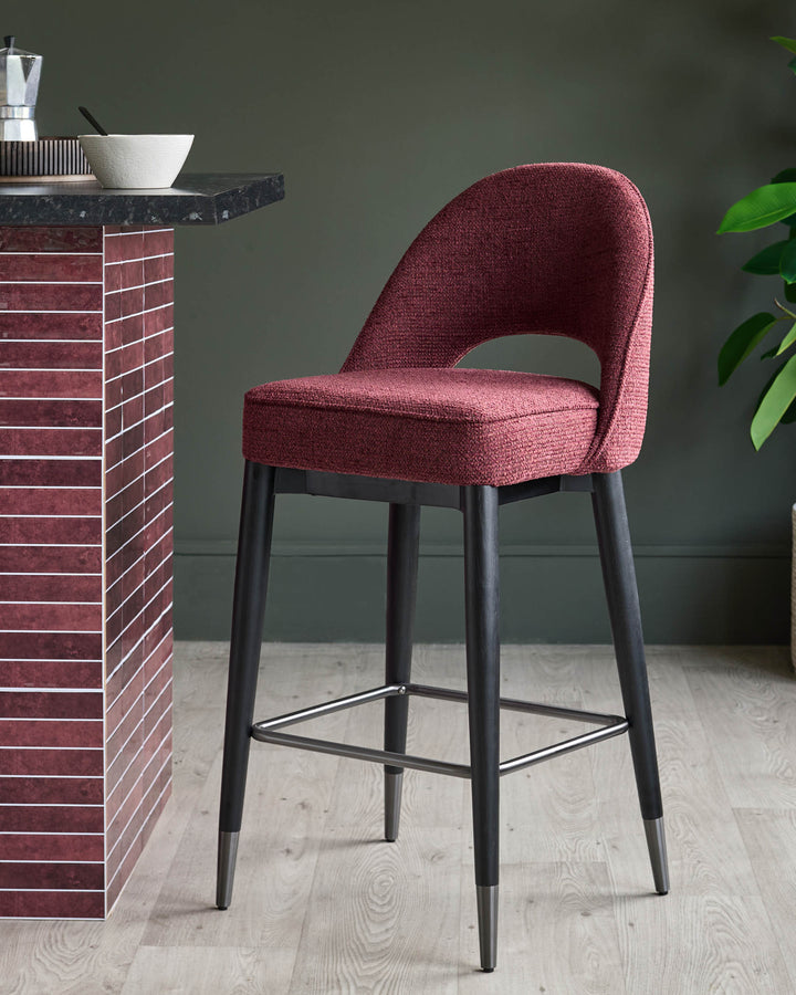 A stylish burgundy bar stool with a curved back, dark wooden legs and a metallic footrest, placed beside a kitchen island.