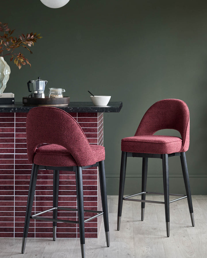 Two burgundy bar stools with black legs sit by a kitchen counter with red tile.