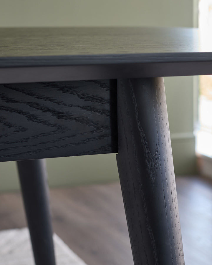 Close-up of black wooden dining table leg and top edge, showing wood grain detail and finish.