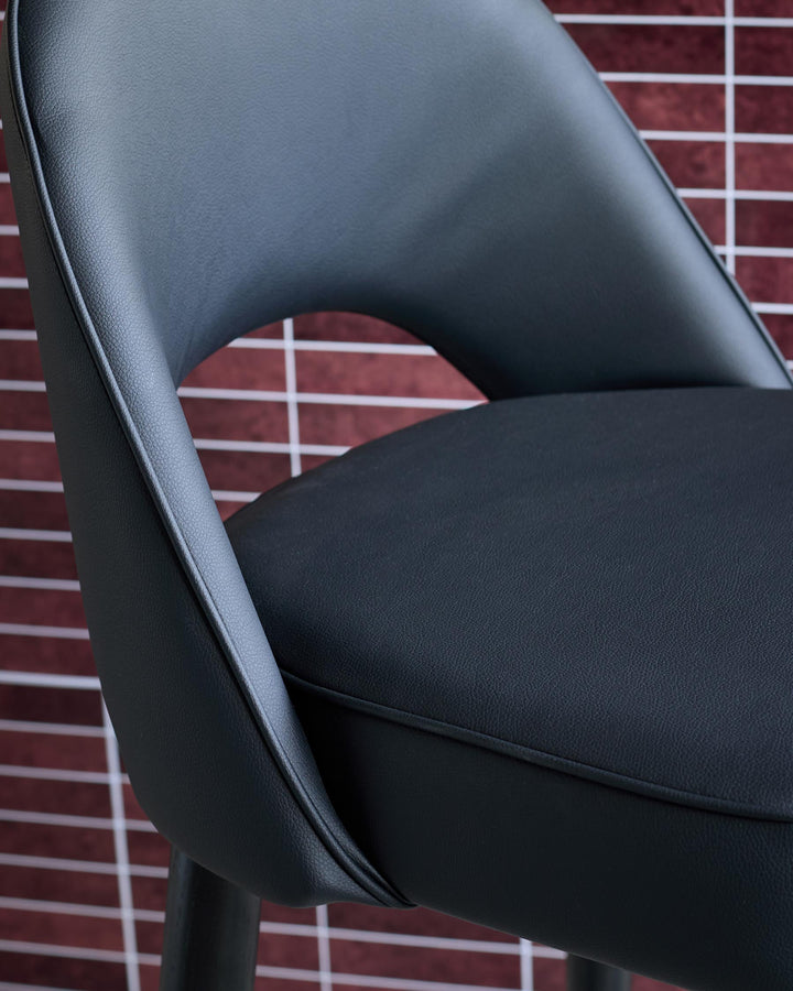 Close-up of a stylish, black leather chair, showing the seat and back against a red tile backdrop.