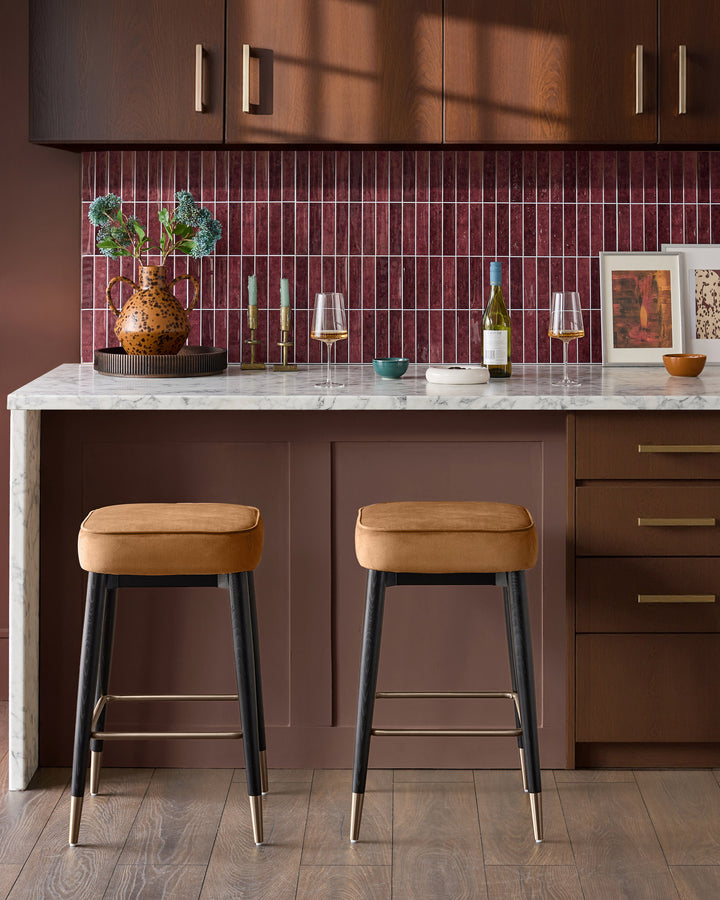 Caramel fabric backless bar stool with black legs and brass footrest, shown at kitchen island.