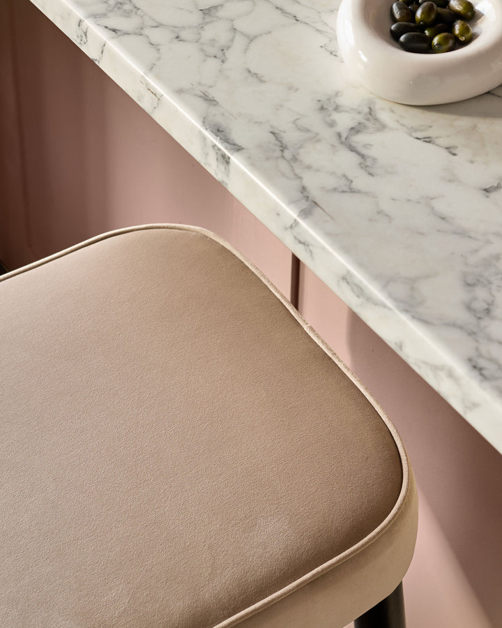 Clover velvet backless bar stool in champagne, shown from side angle near marble countertop with olives bowl.