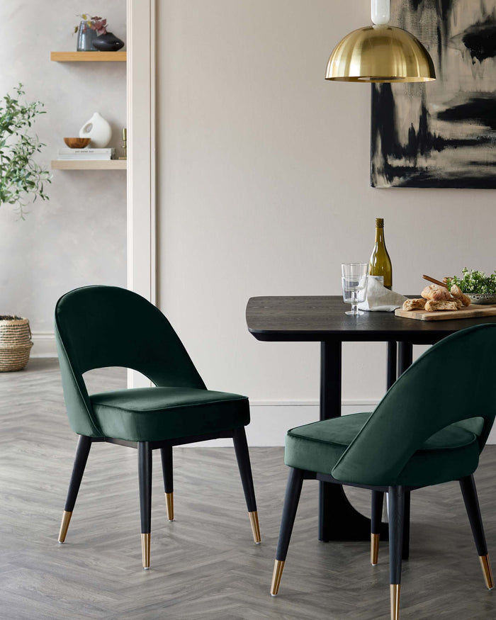 A contemporary dining set with two green velvet chairs and a dark wood table, illuminated by a brass pendant light.