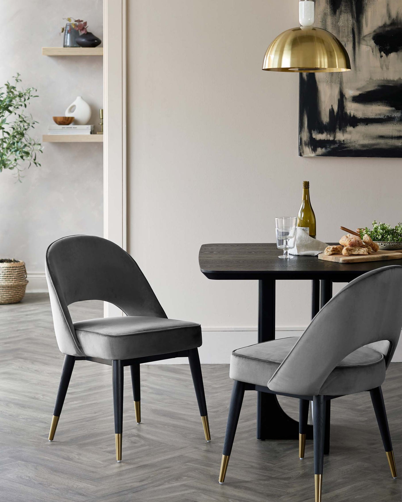 Elegant dining set featuring a rectangular black wooden table with a smooth finish and slim legs, paired with two plush velvet-upholstered chairs with a curved backrest, showcasing a sleek modern design in a grey tone with contrasting black legs tipped with brass accents.