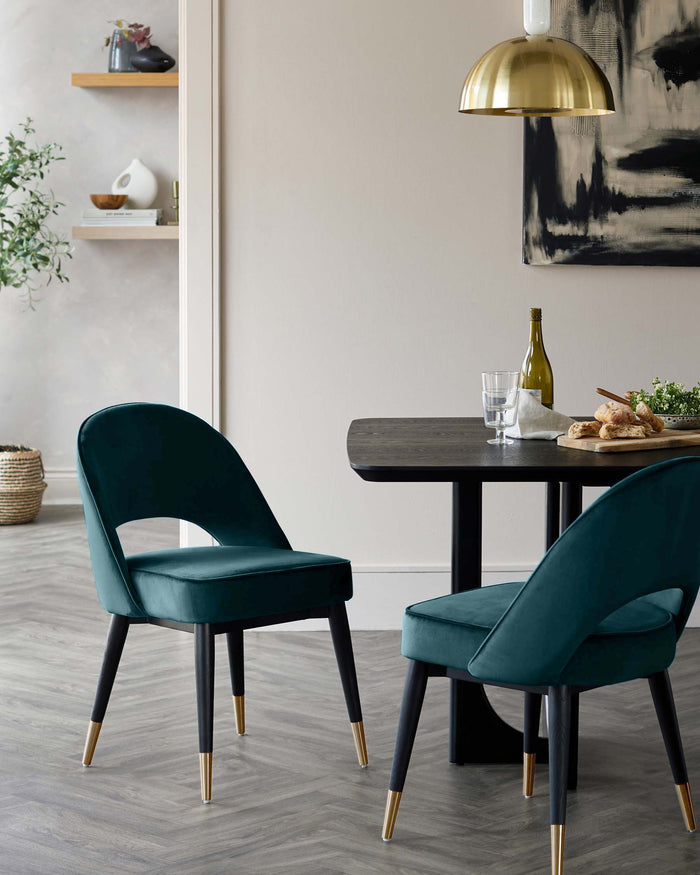 A modern dining set. Includes a dark wooden table and two teal velvet chairs with black legs and gold accents.