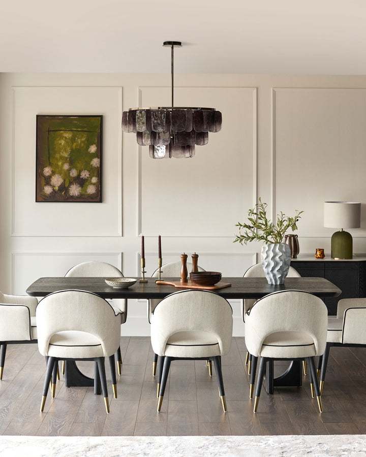 Clover dining armchair in ivory fabric with black legs and brass accents, shown in dining room setting.