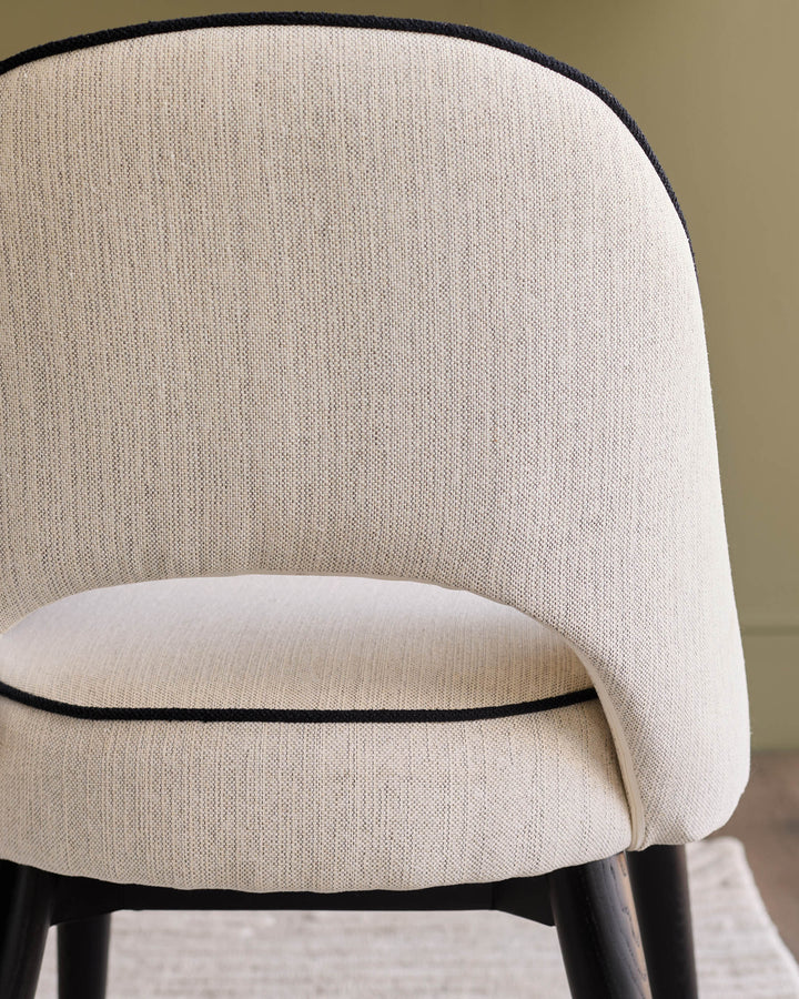 Clover Ivory Fabric Dining Chair - Back view showing curved backrest with black piping trim and dark wooden legs.
