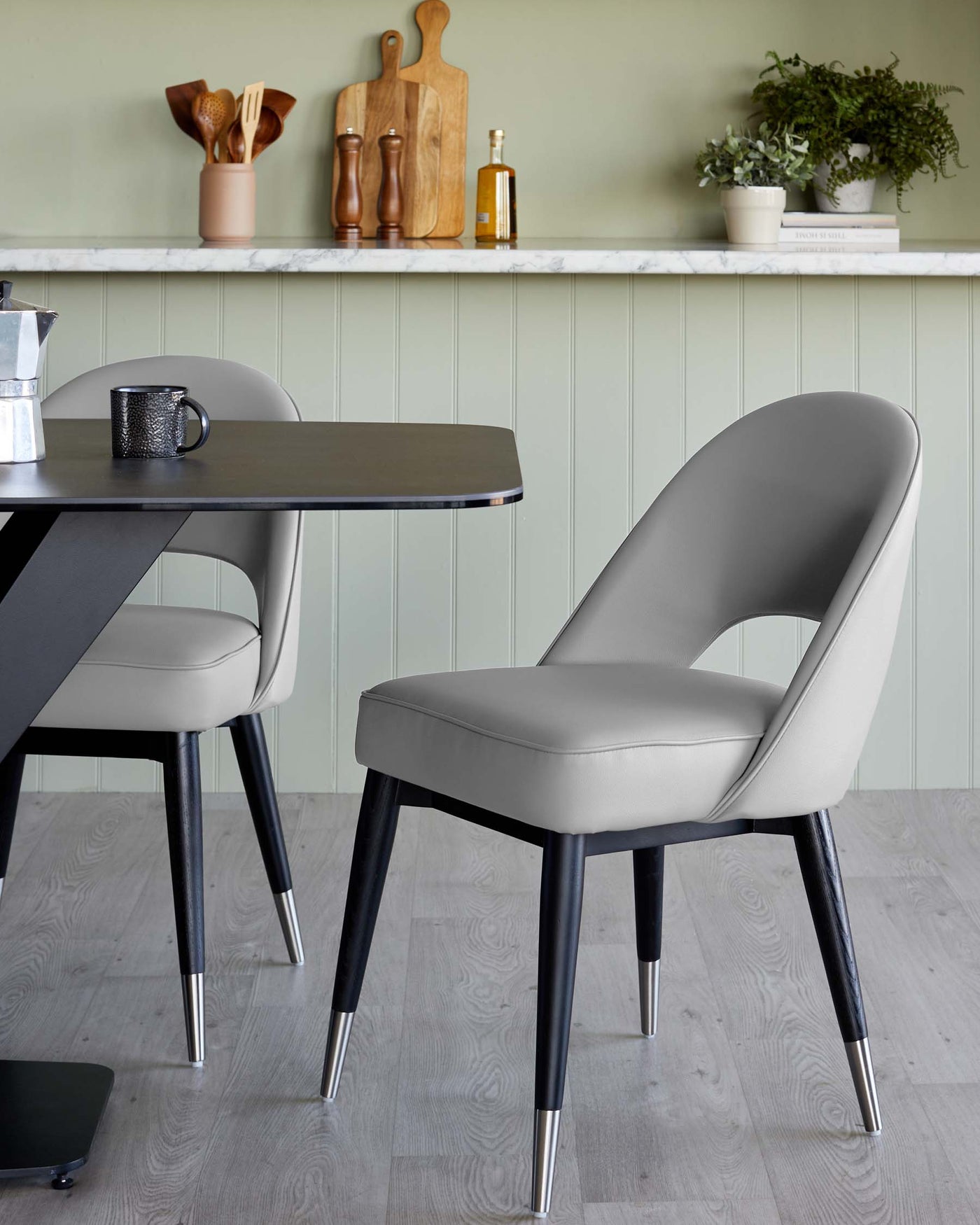 Modern dining set featuring a sleek black rectangular table with metal legs and a complementary elegant grey upholstered dining chair with black and metal accents. The scene is styled in a contemporary dining space with neutral tones.