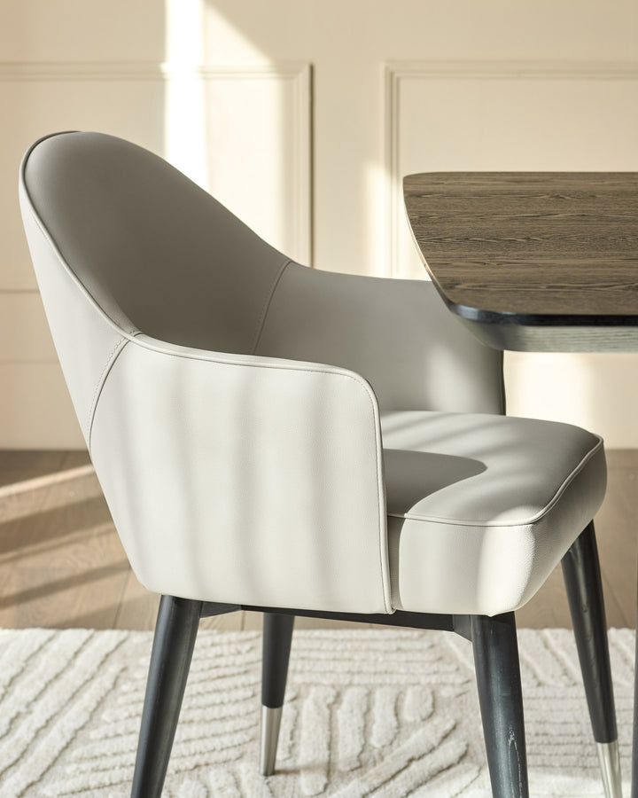 Clover dining armchair in light grey faux leather with black wooden legs, shown from a side angle at a table.