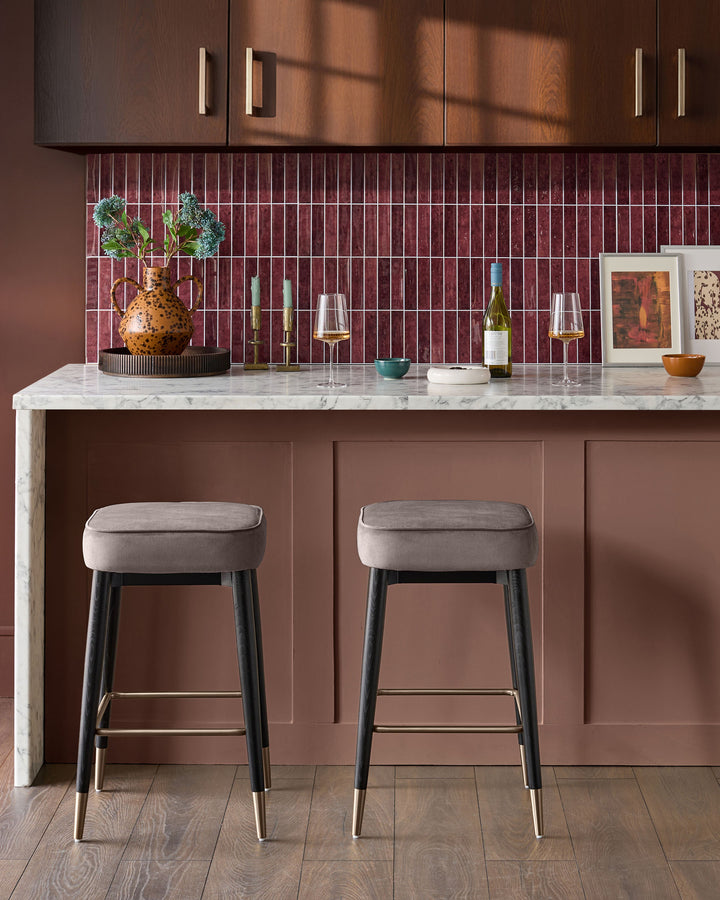 Mocha velvet backless bar stool with black legs and brass footrest, shown at kitchen island with marble countertop.