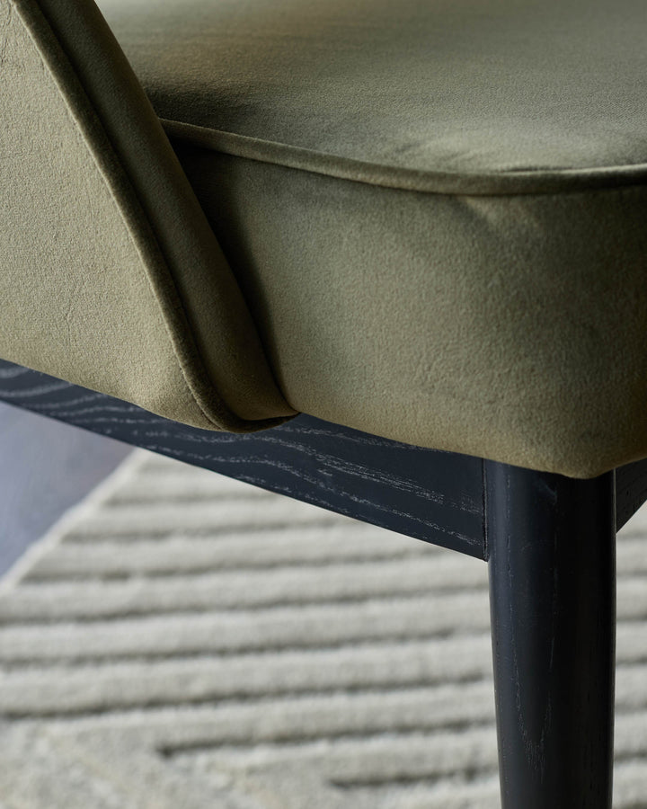 Close-up of a stylish chair with green upholstery and dark wooden legs.